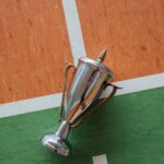 A shiny stainless steel trophy laying on a vibrant sports court surface, ready for a victor.