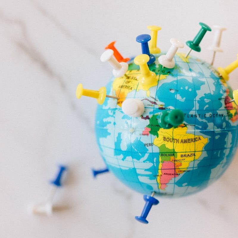 A globe decorated with colorful push pins on a marble surface represents global connections